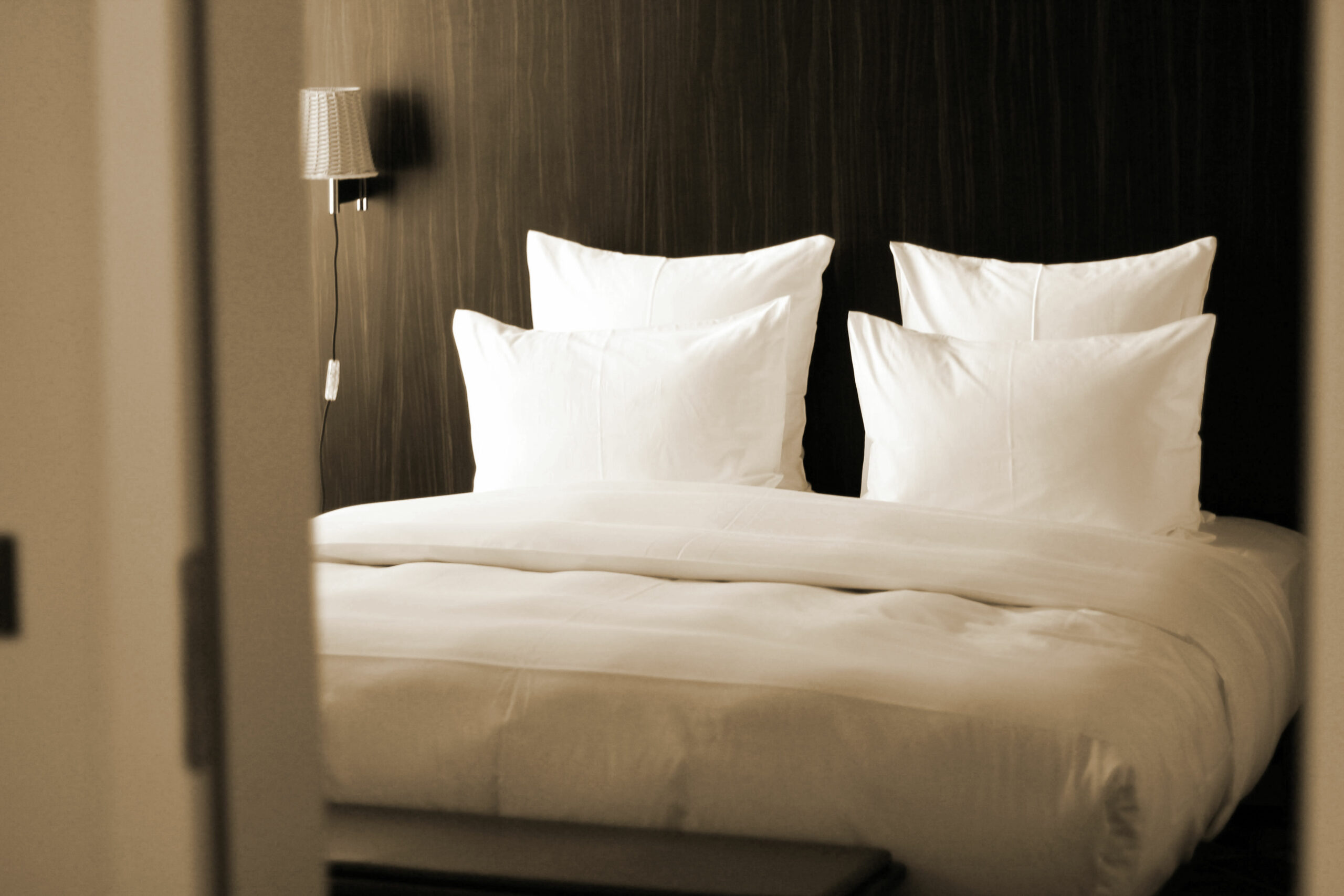Chambre d'hôtel contemporaine vue depuis le couloir, lit double aux oreillers blancs impeccablement disposés sur tête de lit en bois sombre, standards housekeeping du Groupe St Ho