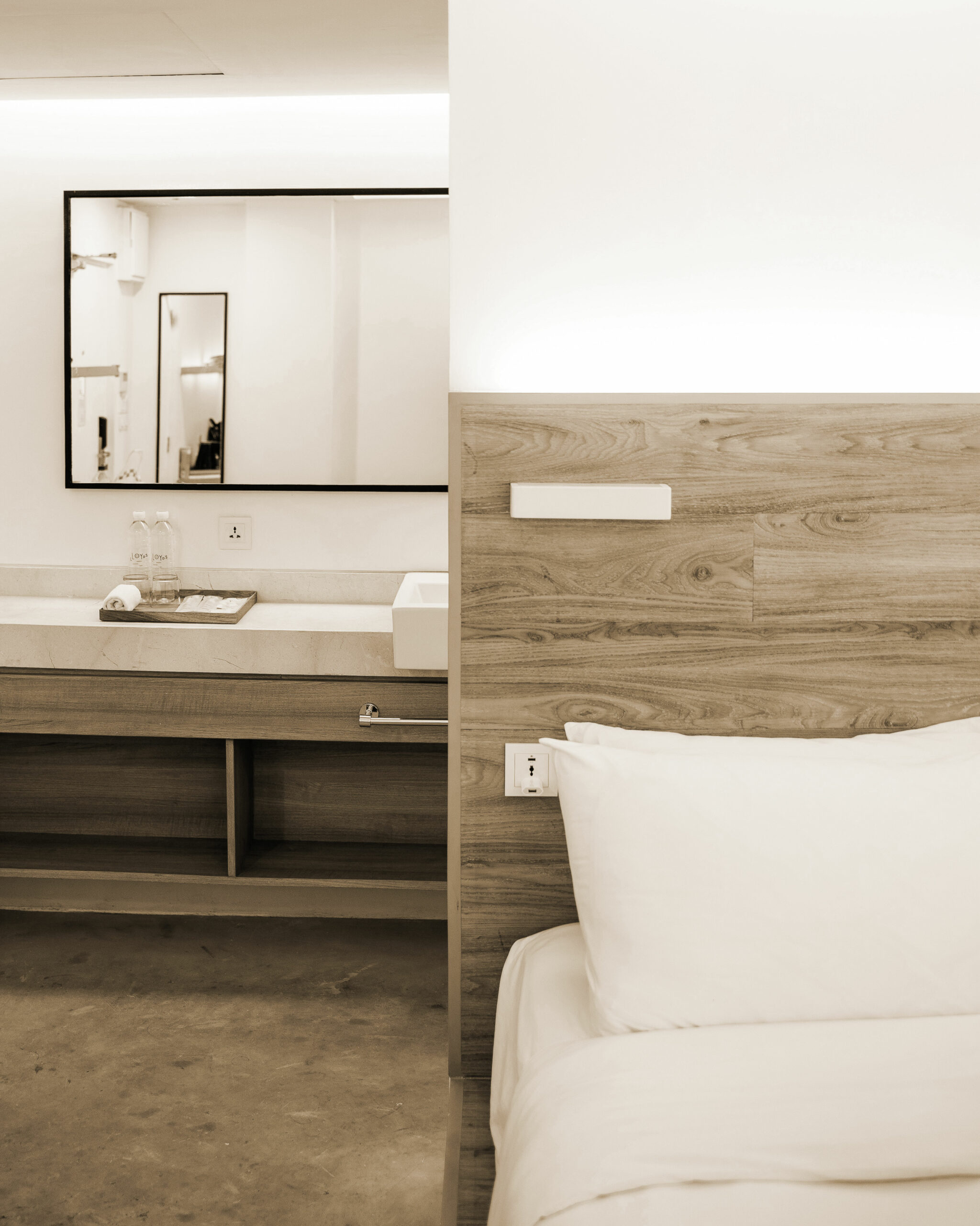 Chambre d'hôtel design avec salle de bain ouverte, tête de lit en bois naturel rétroéclairée, lavabo vasque et oreiller blanc impeccable, housekeeping global du Groupe St Ho