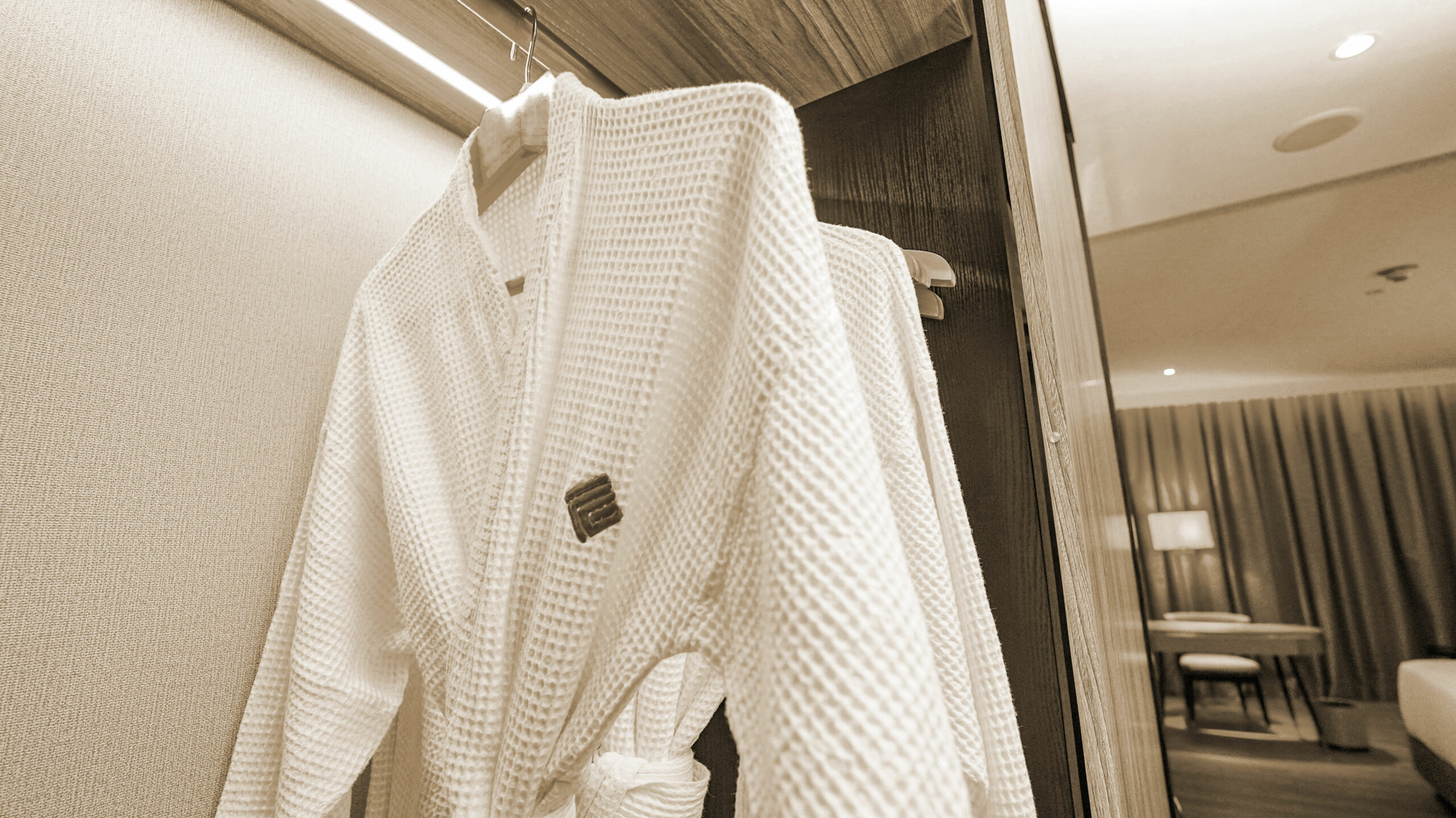 Peignoir en tissu gaufré blanc suspendu sur cintre dans le dressing d'une chambre d'hôtel haut de gamme, mise en place housekeeping soignée