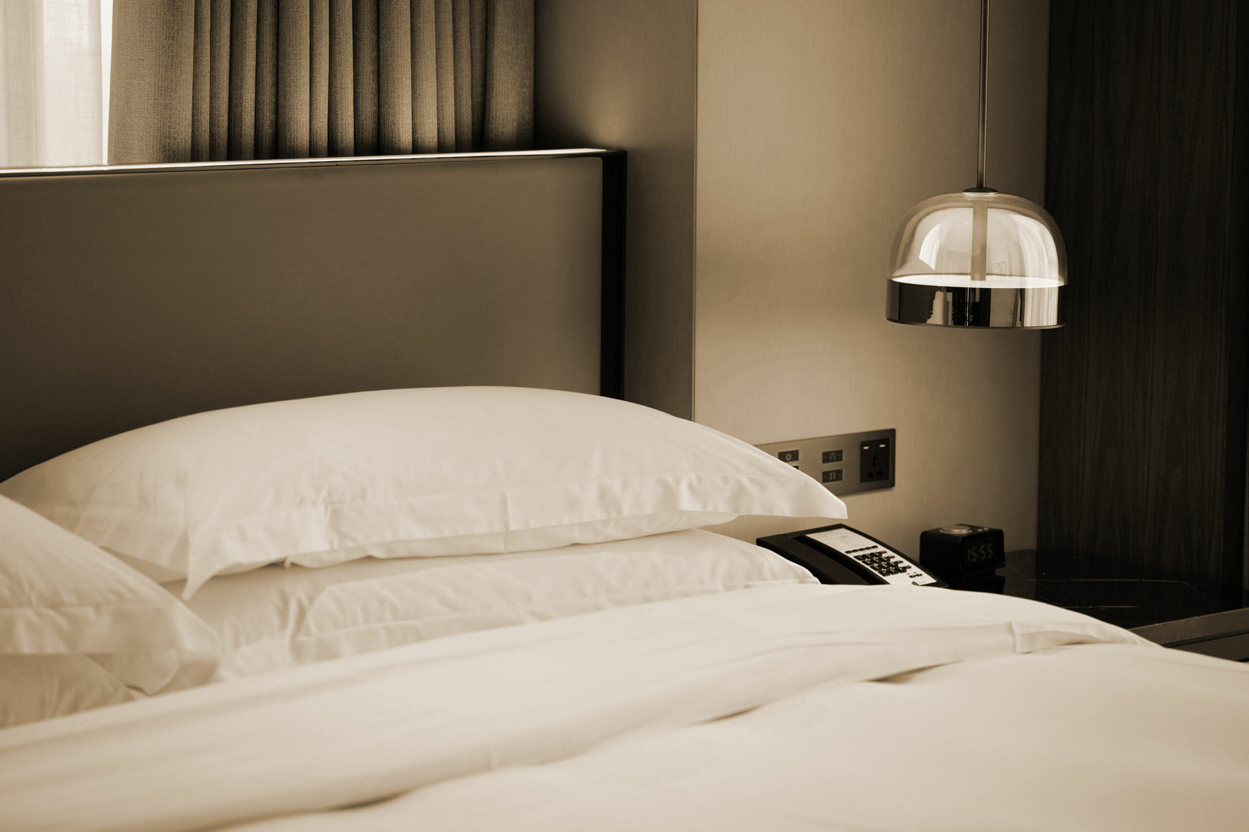 Gros plan sur lit d'hôtel contemporain aux oreillers blancs moelleux, tête de lit grise et suspension chromée design, soin du détail housekeeping
